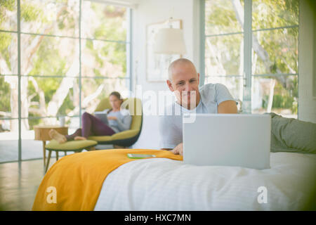Mature couple relaxing, using laptop and digital tablet in bedroom Stock Photo