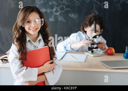 Representing our science project. Happy cheerful capable pupils standing in the lab and exploring science while working on the project and using equip Stock Photo