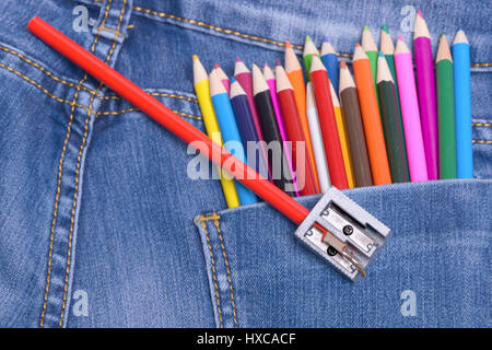 Pocket jeans and a group of colorful drawing pencils. Sharpener and blurry colored pencils in second plan. Stock Photo