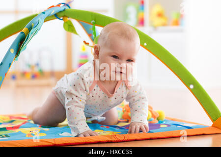 Unhappy seven months baby girl crawling on colorful playmat Stock Photo