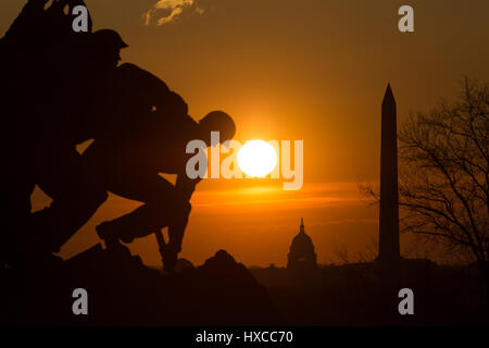 The US Marine Corps War Memorial silhouetted against an orange sky at sunrise, with iconic Washington, DC landmarks in the background. Stock Photo