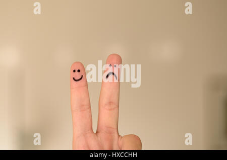 Two hand drawn emoticon faces on a persons fingers , one happy and smiling and the other unhappy, sad or depressed isolated on a neutral background wi Stock Photo