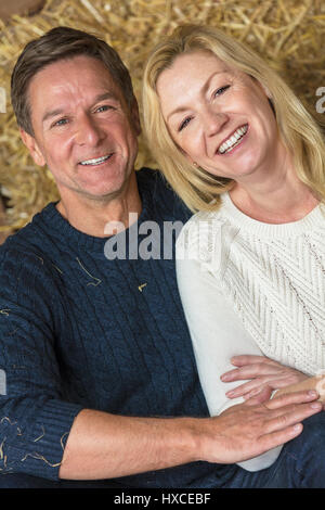 Portrait shot of an attractive, successful and happy middle aged man and woman couple sitting laughing together on hay or straw bales Stock Photo