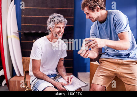 Male surfboard designers with cell phone brainstorming in workshop Stock Photo