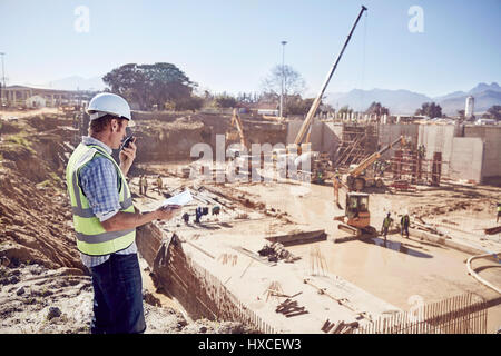 Construction worker foreman using walkie-talkie at sunny construction site Stock Photo