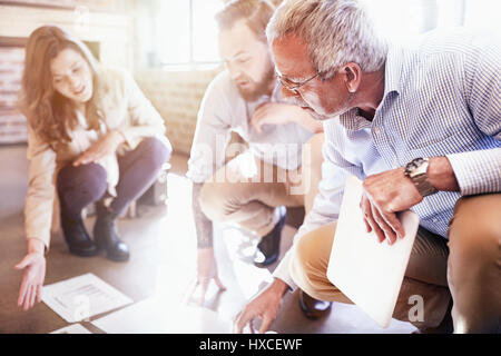 Business people reviewing and discussing paperwork on sunny office floor Stock Photo