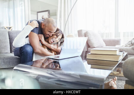 Playful couple hugging and using laptop in living room Stock Photo