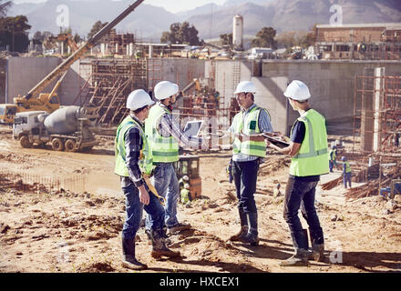 Construction workers and engineers shaking hands, meeting at sunny construction site Stock Photo