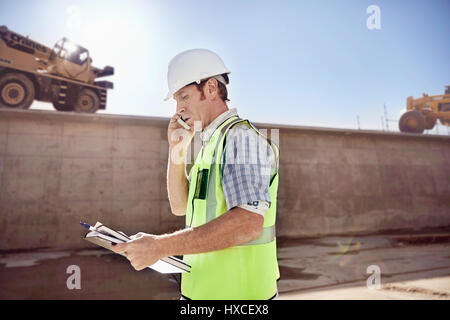 Construction worker foreman talking on cell phone at sunny construction site Stock Photo