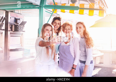 Young women taking selfie with senior business owner outside sunny food cart Stock Photo