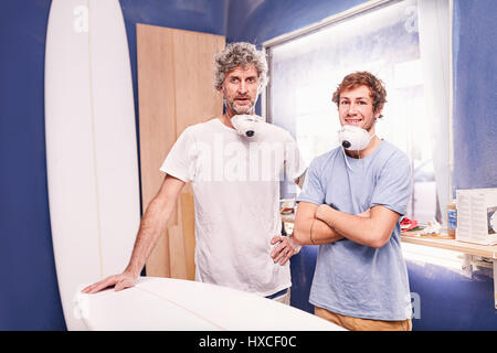 Portrait confident male surfboard designers with protective masks in workshop Stock Photo