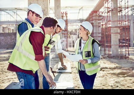 Female foreman talking to construction workers at sunny construction site Stock Photo
