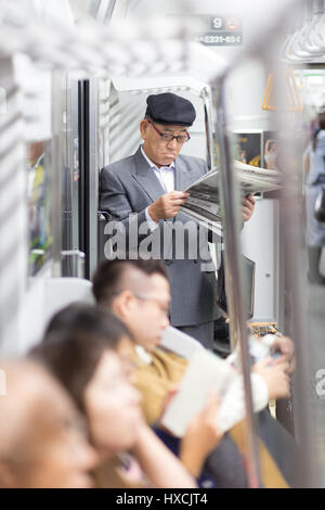Japanese businessman taking ride to work in morning, standing inside public transport and reading newspaper. Stock Photo