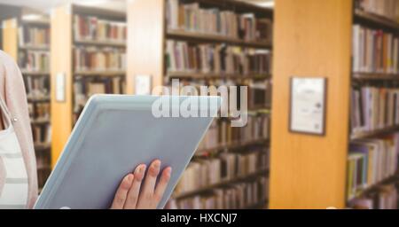 Digital composite of womans hands on tablet in Library Stock Photo