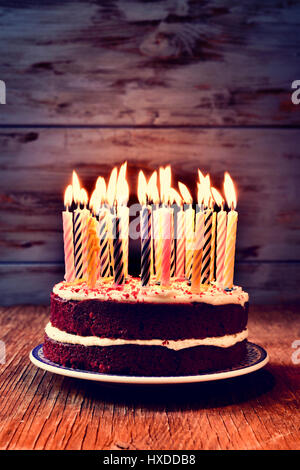 a cake topped with some lit candles before blowing out the cake, on a rustic wooden table, against a blue wooden background Stock Photo