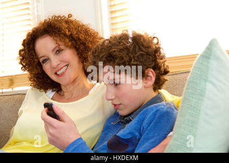 Portrait of a cheerful mother sitting next to her son who is playing games on his phone Stock Photo