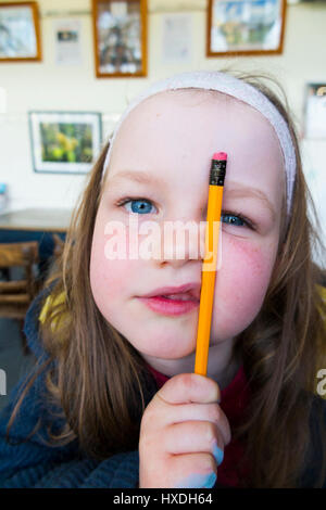 Face / portrait head shot of four 4 / five 5 year old school aged girl / kid with pencil and rubber eraser, and showing slight defiance. UK Stock Photo