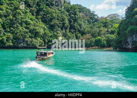 Long boat drives towards beach and coastal forest. Stock Photo