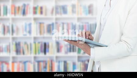 Digital composite of Womans hands on tablet in Library Stock Photo