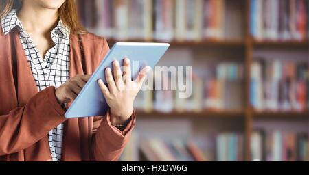 Digital composite of Womans hands on tablet in Library Stock Photo