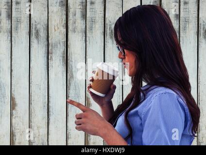 Digital composite of Woman drinking from coffee cup and pointing against wood panel Stock Photo