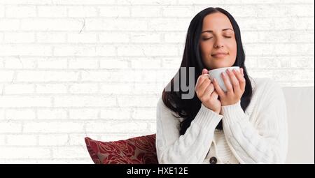 Digital composite of Woman on couch with white mug against white brick wall Stock Photo