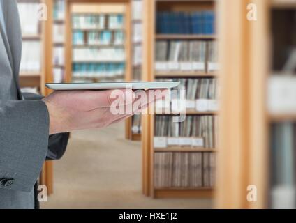 Digital composite of mans hands holding tablet in Library Stock Photo