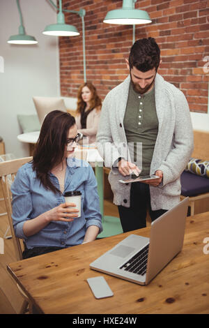Male and Female executives discussing over digital tablet at desk in office Stock Photo