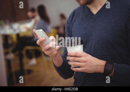 Male executive using mobile phone while having coffee in office Stock Photo
