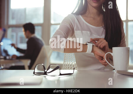 Female executive using smartwatch at desk in office Stock Photo