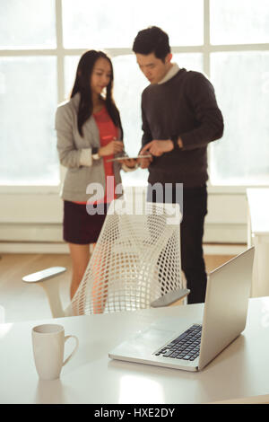 Male and female executives discussing over digital tablet at desk in office Stock Photo