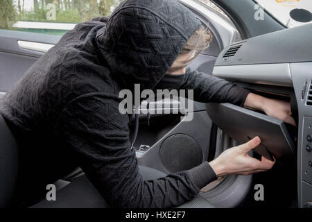 Masked teenage criminal stealing from a car Stock Photo