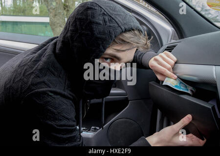 Masked teenage criminal stealing from a car Stock Photo