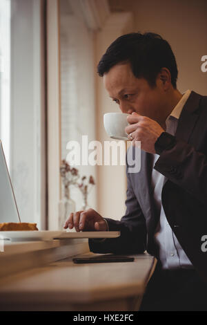 Businessman drinking coffee while using laptop in cafe Stock Photo