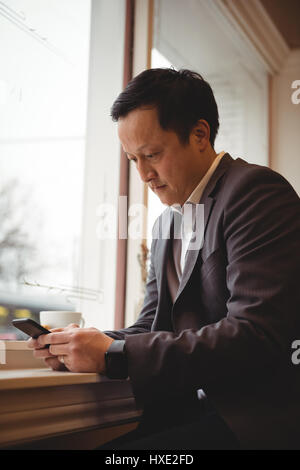 Businessman using mobile phone while sitting by window in coffee shop Stock Photo