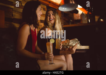 Beautiful women using mobile phone while having cocktail in bar Stock Photo