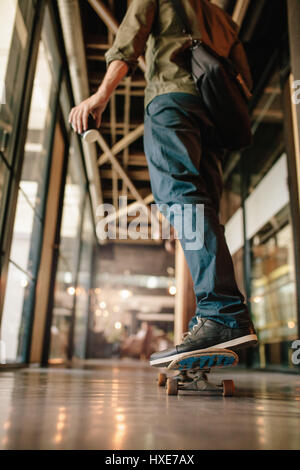 Rear view shot of man skateboarding in office corridor. Young businessman skating through his startup office. Stock Photo