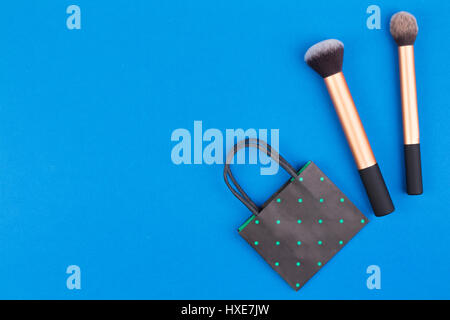 Make up brushes with black polka dot paper shopping bag on blue background. Top view. Flat lay. Stock Photo