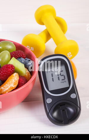 Fresh fruit salad, glucose meter with result of sugar level and dumbbells for fitness, concept of diabetes, sport, diet, slimming, healthy lifestyles  Stock Photo