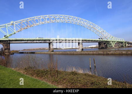 The Silver Jubilee Bridge at Runcorn crossing the Manchester Ship Canal and the River Mersey. Rail bridge of stone construction with pillars is behind