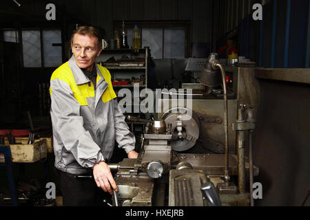 St. Petersburg, Russia - December 23, 2011: Elderly turner turned parts using an outdated lathe turning shop maintenance station forklifts. Stock Photo