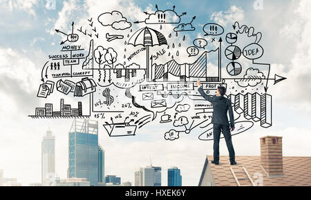 Rear view of businessman on house roof drawing his new business  Stock Photo