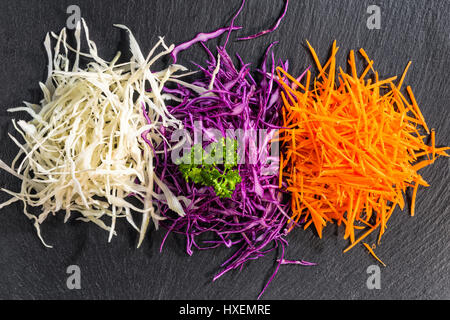 flat lay of mix finely chopped white, red cabbage, carrot decorated parsley on black slate stone background, concept healthy eating Stock Photo