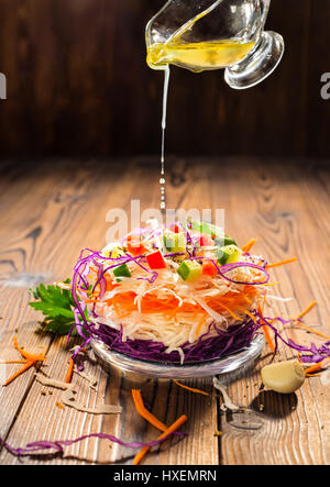 concept of raw food like sandwich with white, red cabbage, carrot decorated red pepper and cucumber pouring with olive oil over wooden table, close up Stock Photo