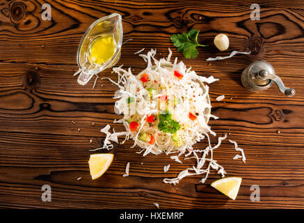 Hand seasoning with a black pepper shaker a fresh salad bowl mixed green  leaves, eggs, black olives and tomato on a wooden table with cutlery.  Nature blurred background. Vertical photography Stock Photo