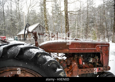 Rusted red tractor in the snow on a New England farm Stock Photo