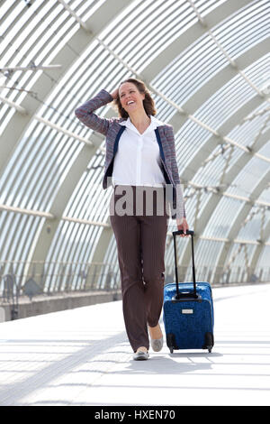 Full body portrait of a business woman smiling and walking at station with bag Stock Photo