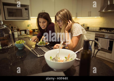 Happy friends using laptop while having breakfast in kitchen at home Stock Photo