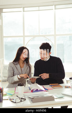Male and Female executives discussing over digital tablet at desk in office Stock Photo