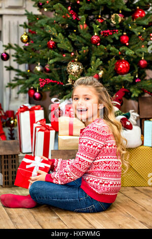 Happy kid sitting on floor with Christmas gift box in hands Stock Photo